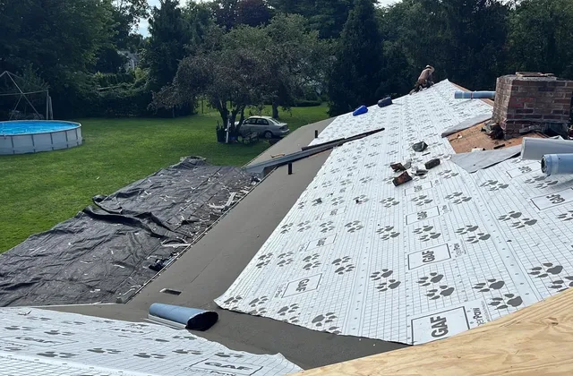 Roof replacement in progress on a Monmouth County NJ home, old shingles torn off to the deck with new underlayment and a brick chimney visible