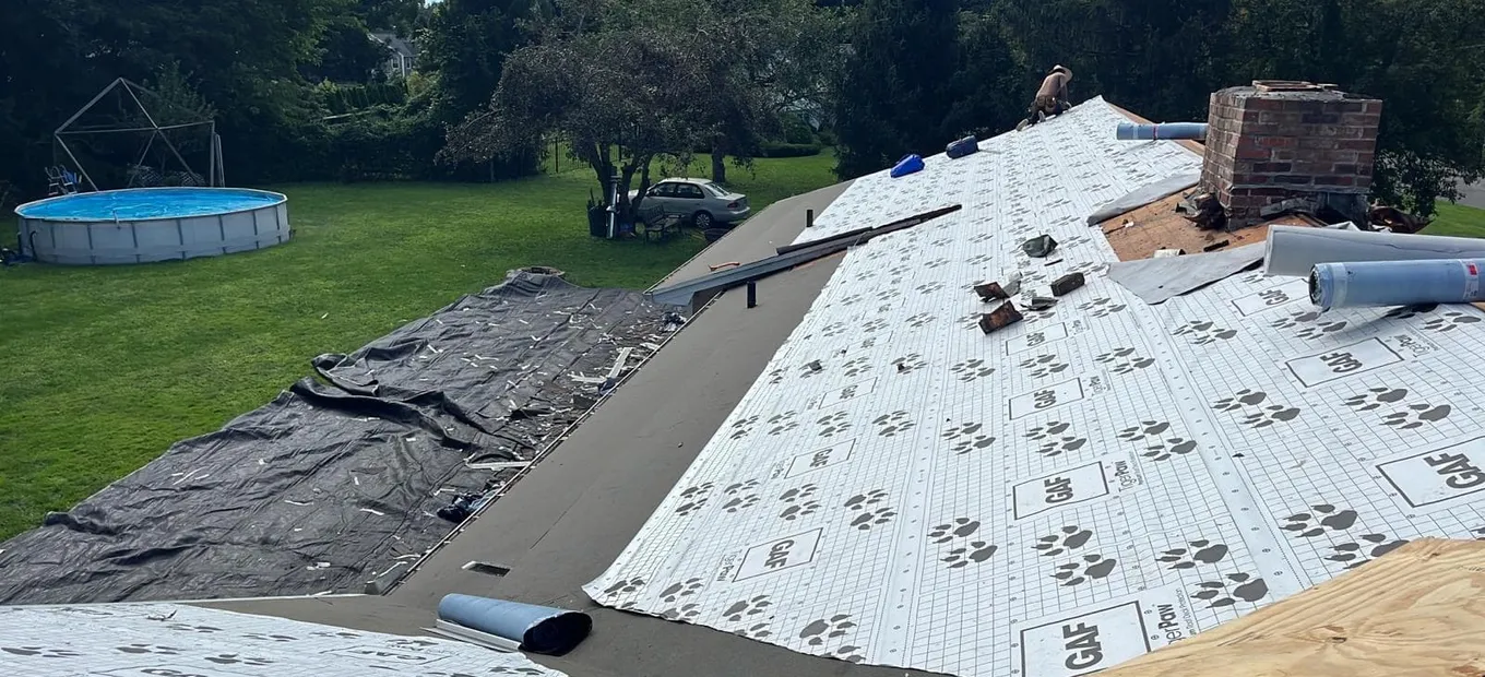 Roof replacement in progress on a Monmouth County NJ home, old shingles torn off to the deck with new underlayment and a brick chimney visible